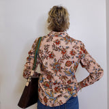 Person wearing a floral shirt and blue jeans against a white wall