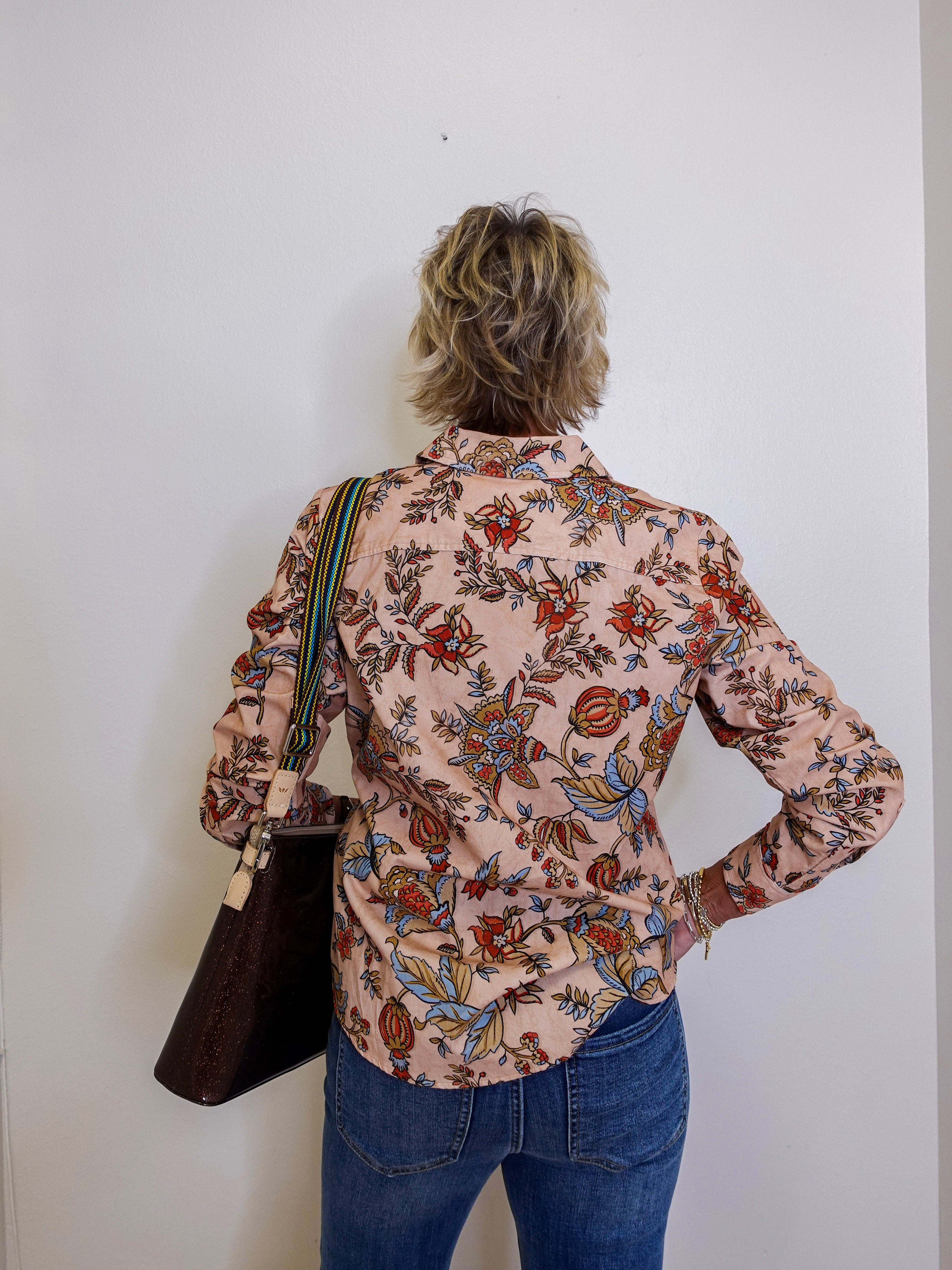 Person wearing a floral shirt and blue jeans against a white wall