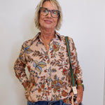Woman wearing a patterned shirt and glasses, holding a bag against a white background