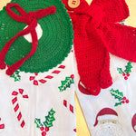 Crocheted Christmas decorations including a green wreath and red bow on a fabric background with holiday patterns.