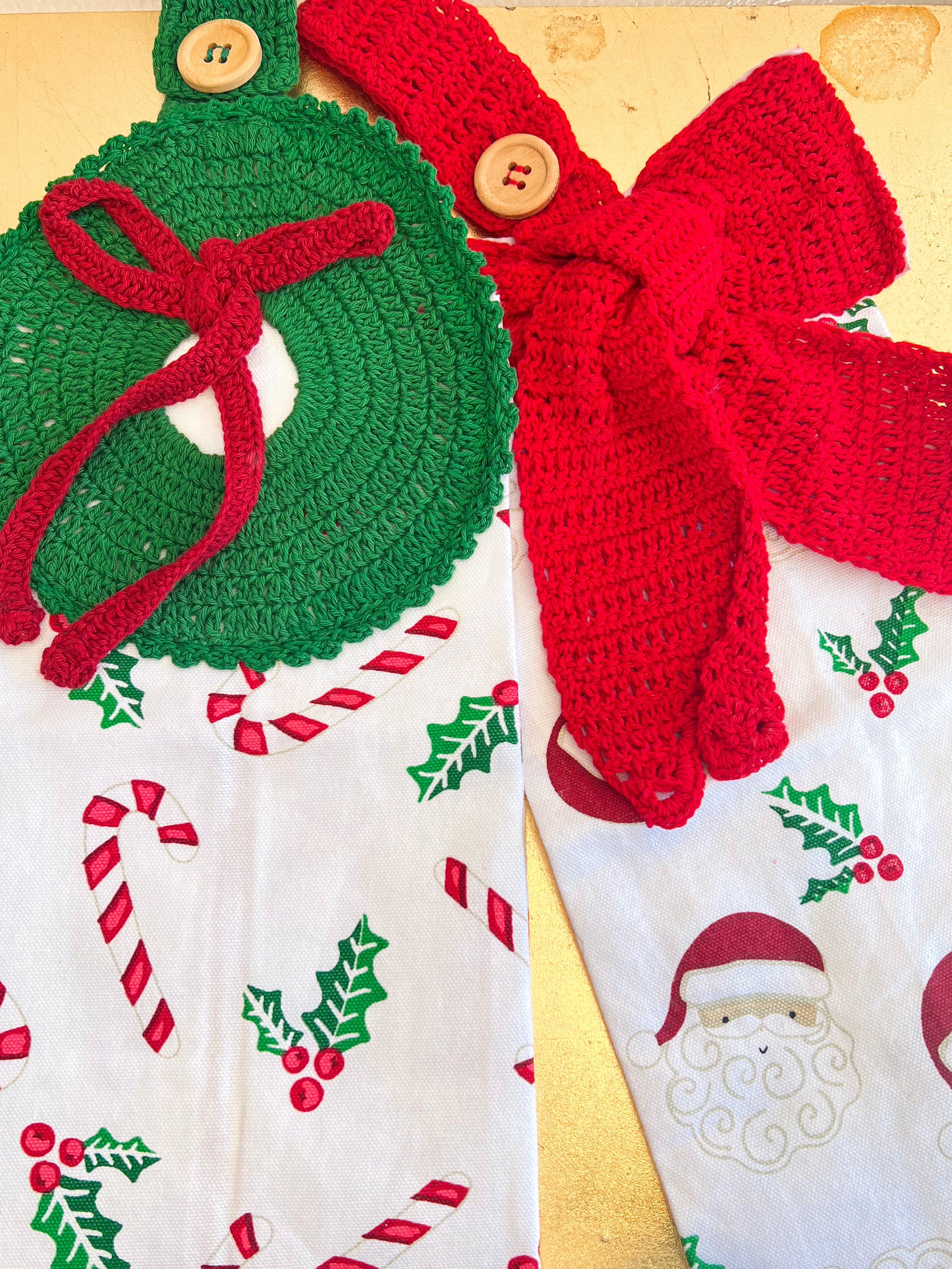 Crocheted Christmas decorations including a green wreath and red bow on a fabric background with holiday patterns.