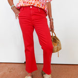 Person wearing a colorful floral blouse and red pants, holding a brown handbag on a white background.