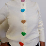 White sweater with colorful heart buttons worn by a person against a white background