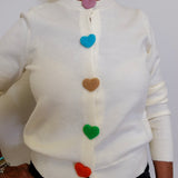 White sweater with colorful heart buttons worn by a person against a white background