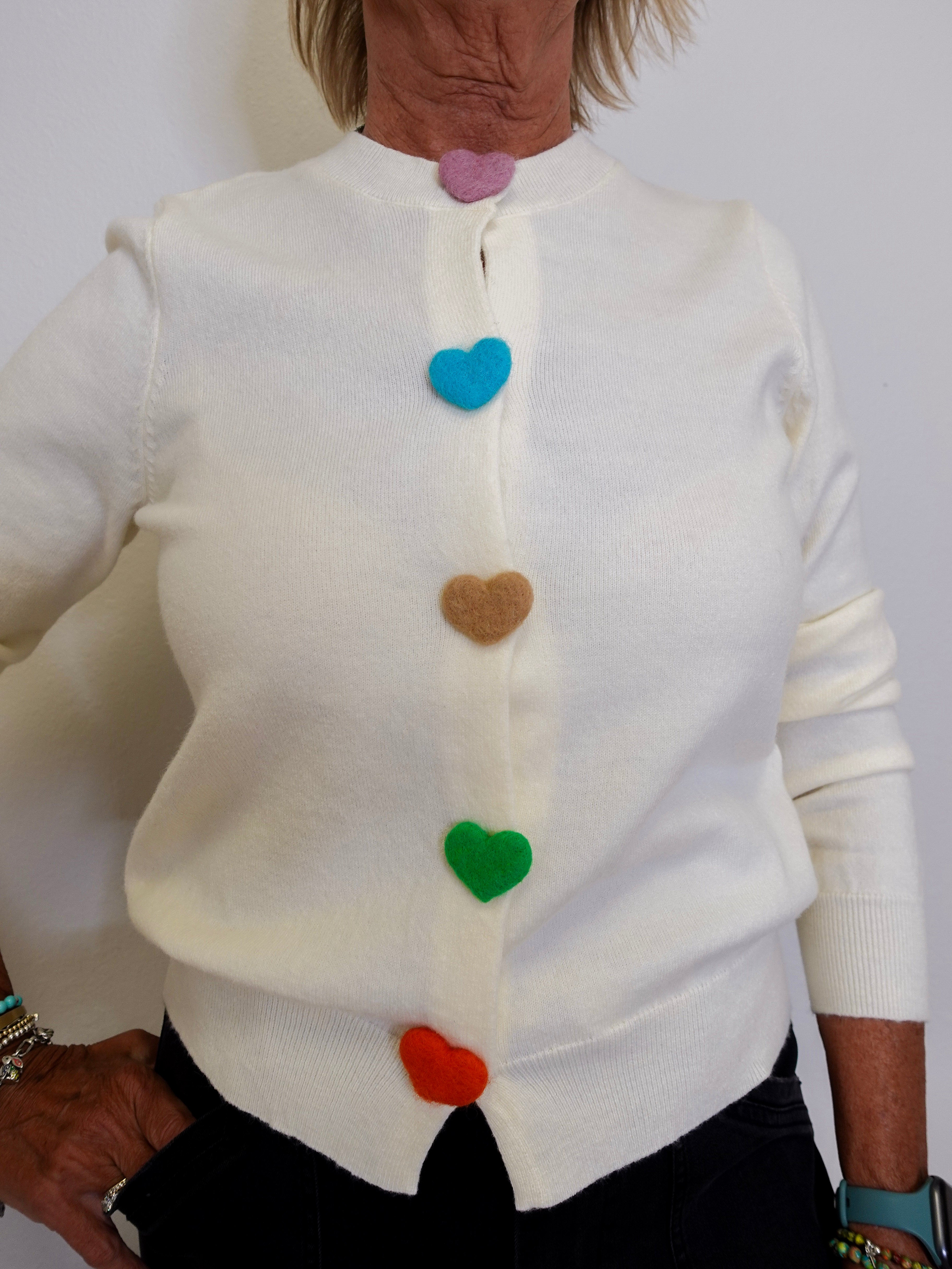 White sweater with colorful heart buttons worn by a person against a white background