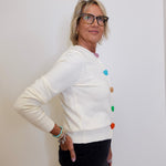 Woman wearing a white sweater with colorful buttons against a plain background