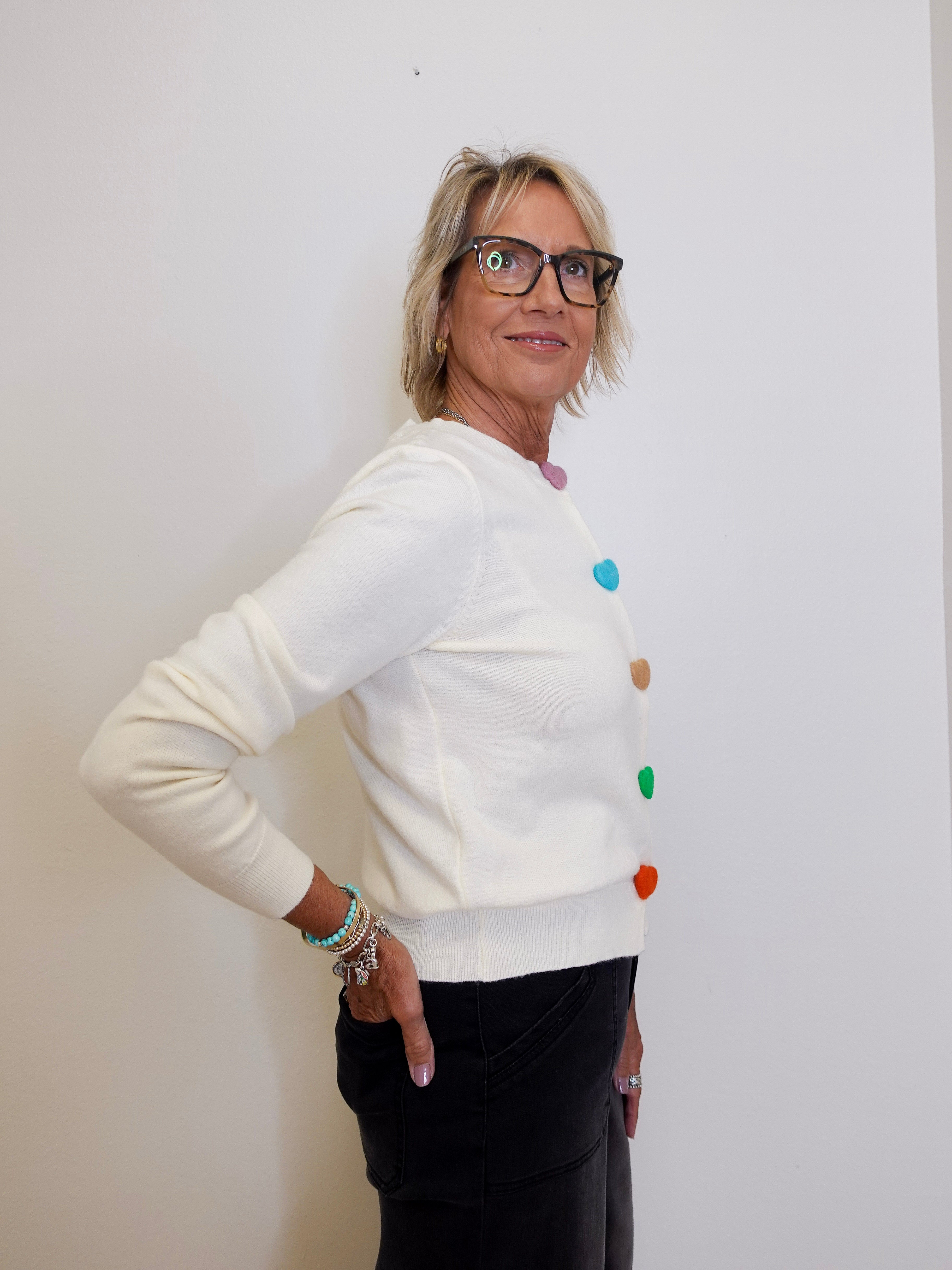 Woman wearing a white sweater with colorful buttons against a plain background