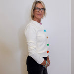 Woman wearing a white sweater with colorful buttons against a plain background