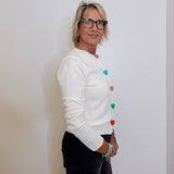 Woman wearing a white sweater with colorful buttons against a plain background