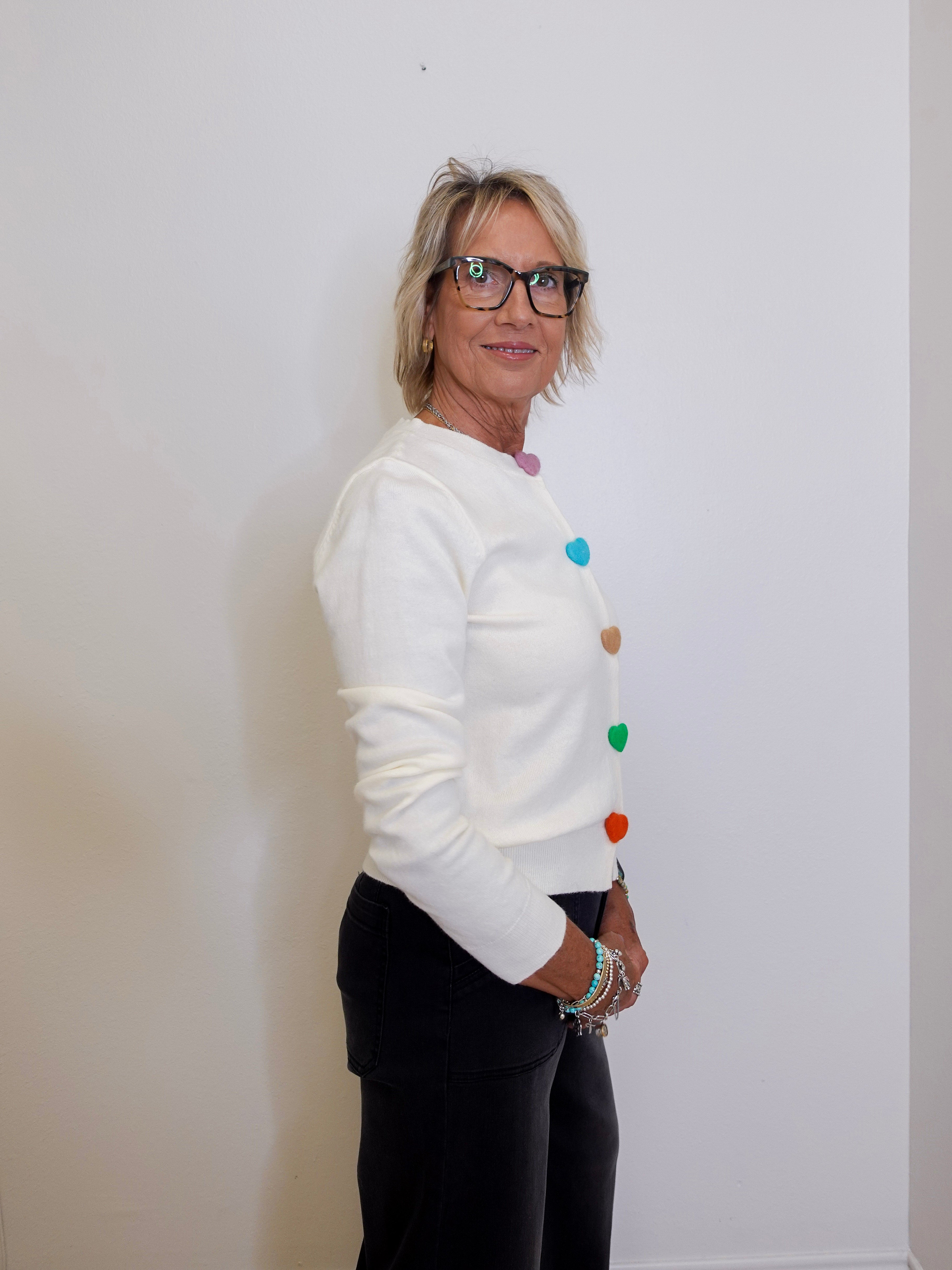 Woman wearing a white sweater with colorful buttons against a plain background