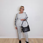 Woman in gray tracksuit holding a black handbag against a white wall