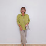Woman wearing a green shirt and beige pants against a white wall