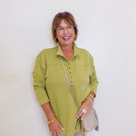 Woman wearing a green sweater top in front of a white wall.

