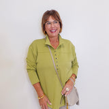 Woman wearing a green sweater top in front of a white wall.
