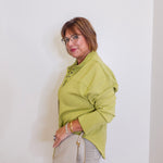 Woman wearing a green jacket and beige pants against a white wall