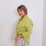 Woman wearing a green jacket and beige pants against a white wall