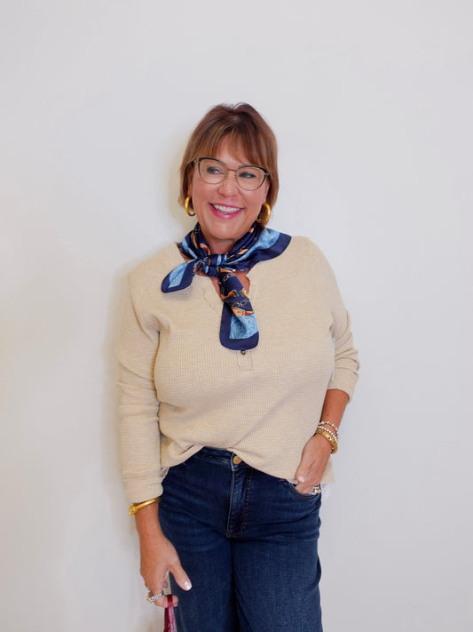 woman wearing a henley top with buttons that is tan in front of a white background. 