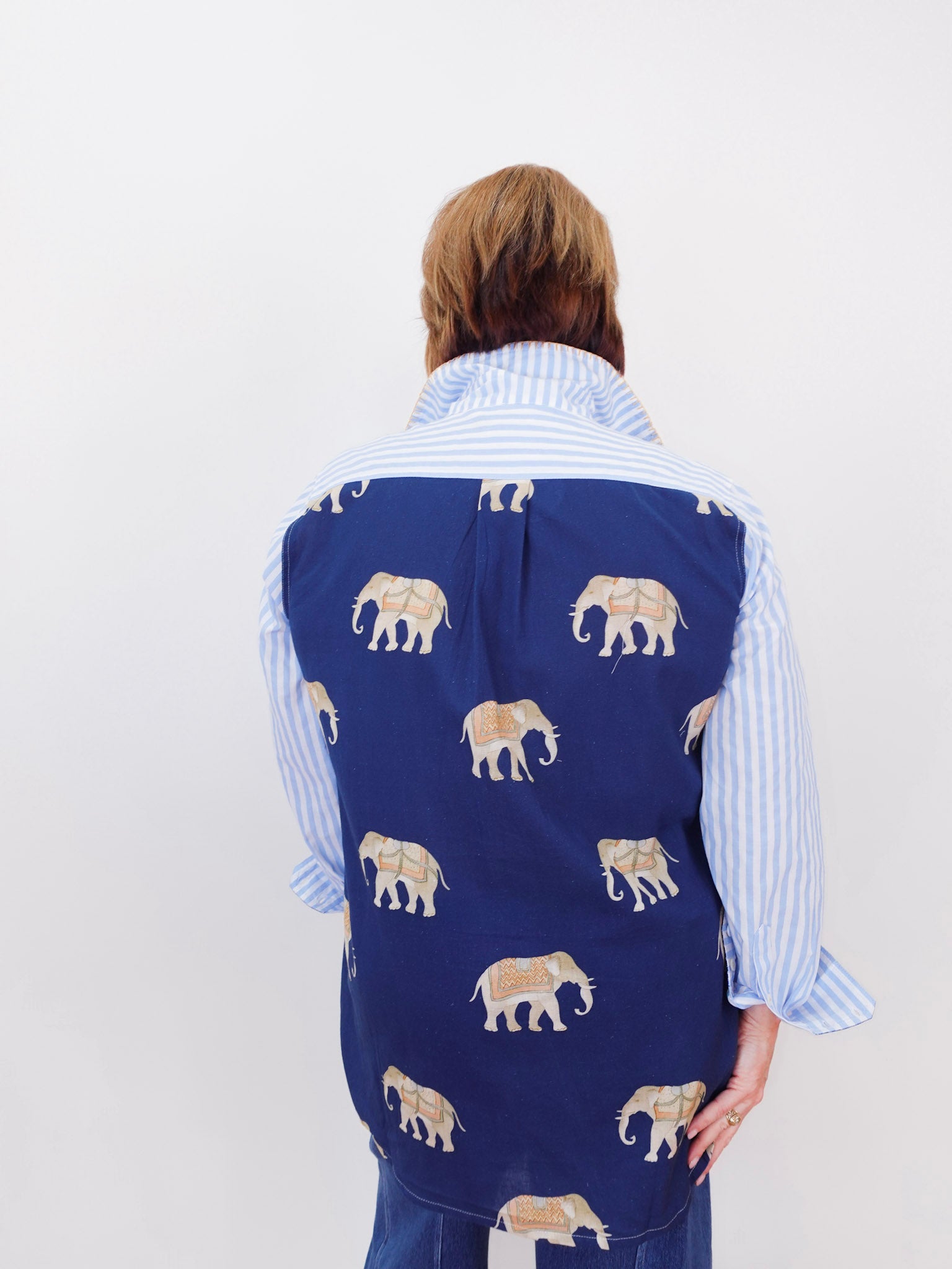 Person wearing a blue vest with elephant pattern over a striped shirt on a white background