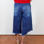Person wearing blue denim culottes and a red top on a white background