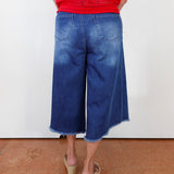 Person wearing blue denim culottes and a red top on a white background