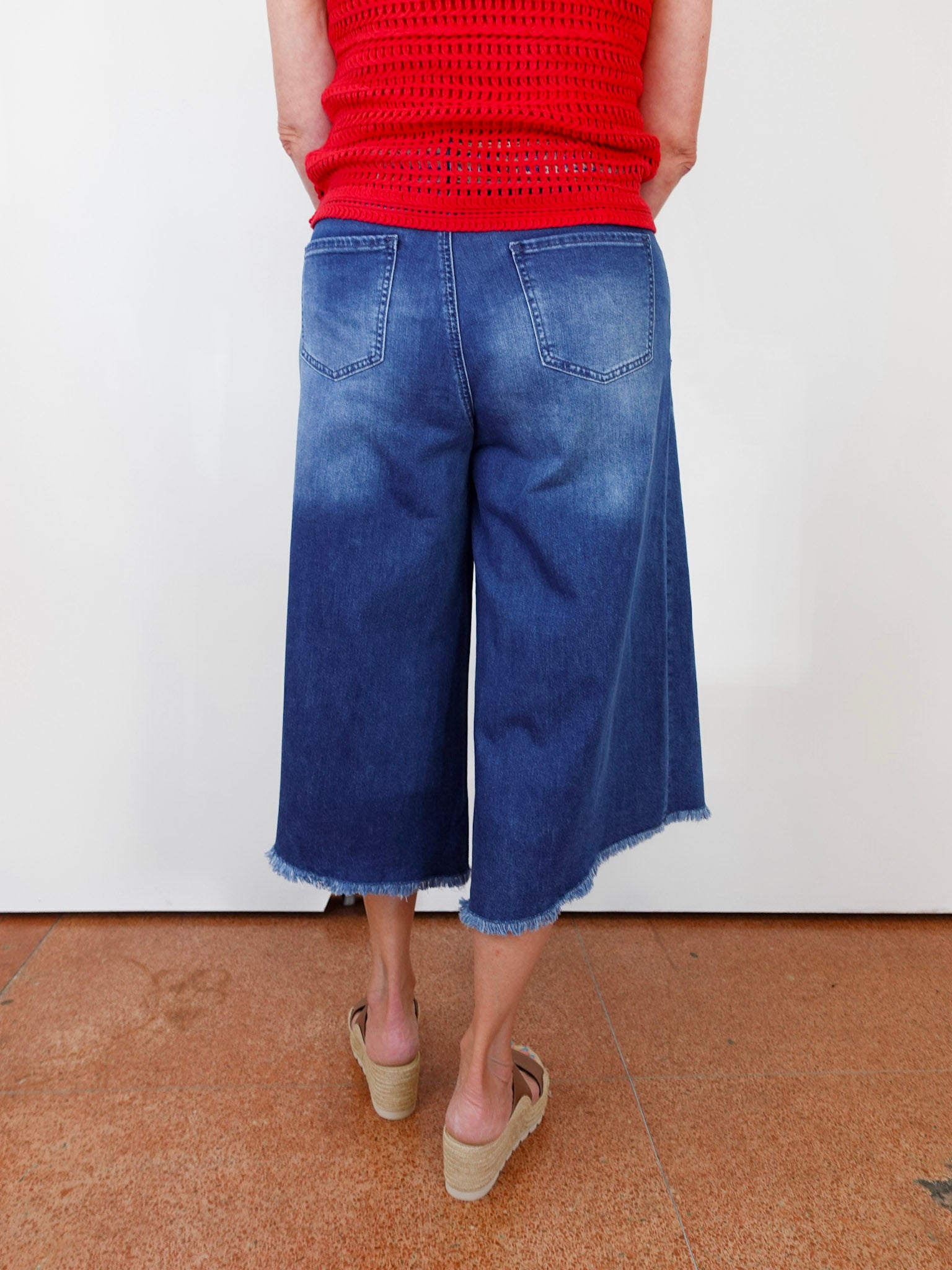Person wearing blue denim culottes and a red top on a white background