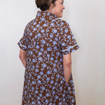 Woman wearing a brown floral dress against a white wall