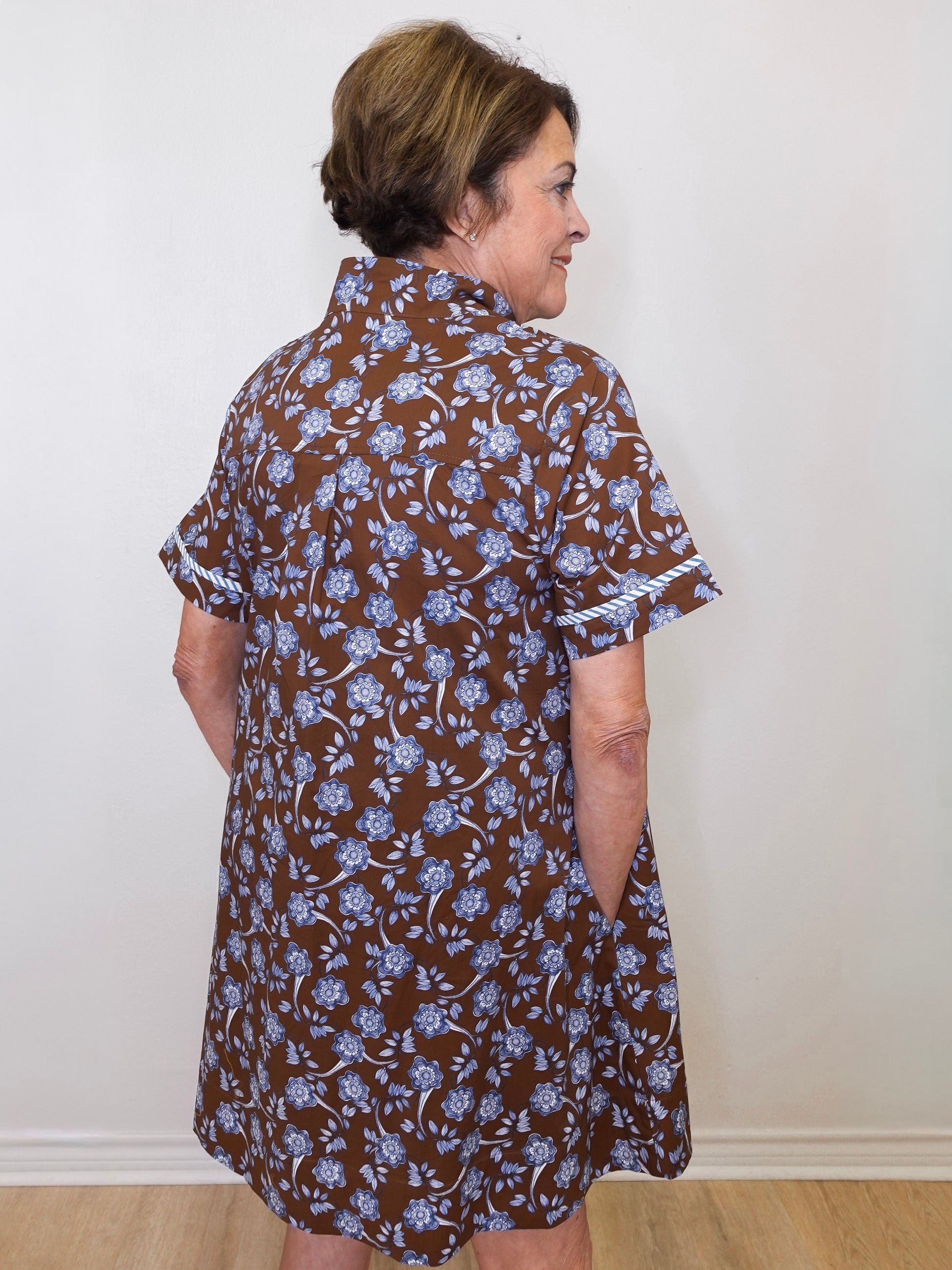 Woman wearing a brown floral dress against a white wall
