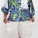 Person wearing a tropical leaf pattern shirt and white shorts on a plain background