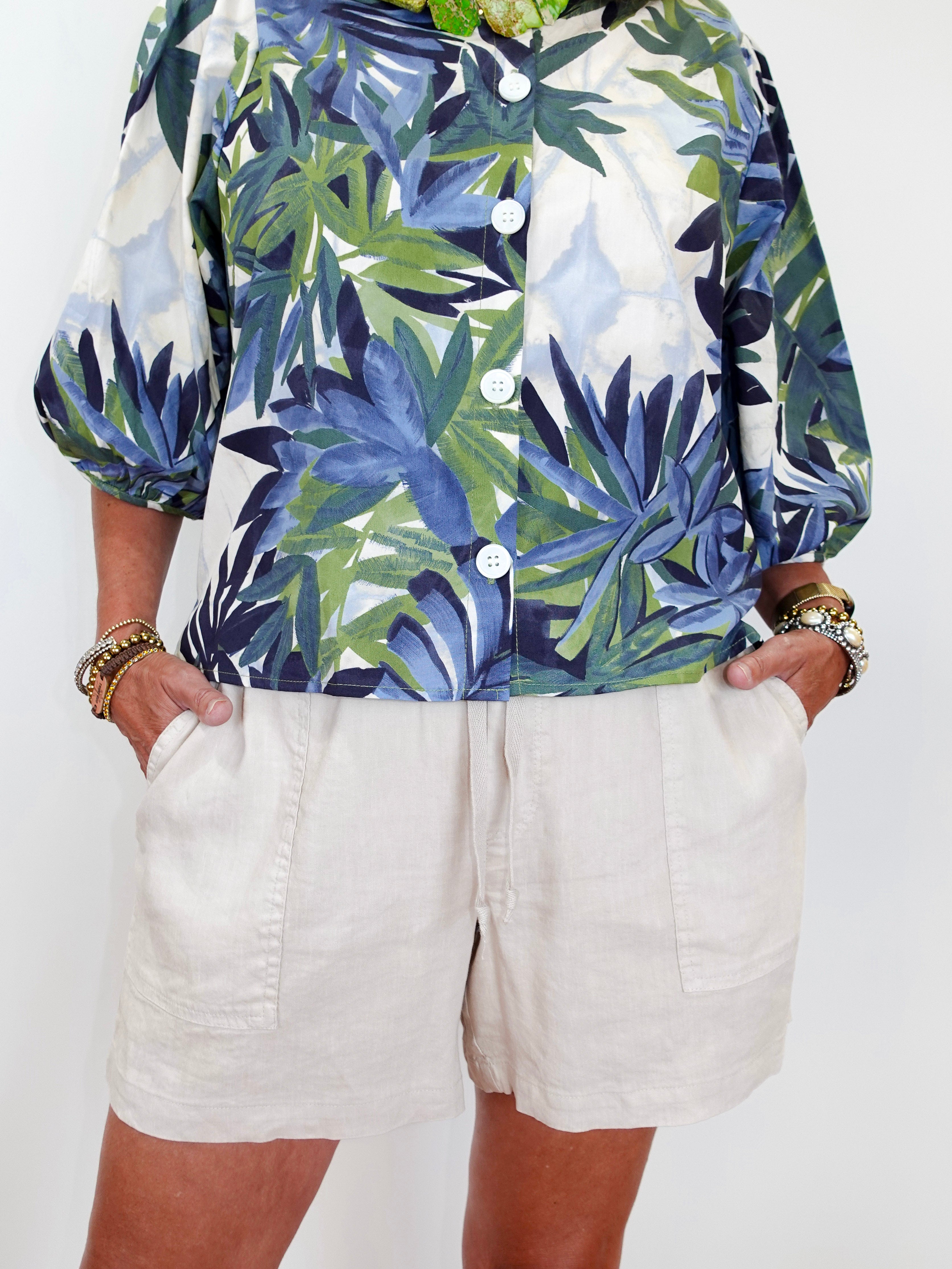 Person wearing a tropical leaf pattern shirt and white shorts on a plain background
