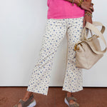 Person wearing a pink top and floral pants, holding a beige handbag on a white background