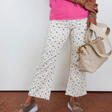 Person wearing a pink top and floral pants, holding a beige handbag on a white background