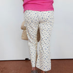 Person wearing a pink top and white floral pants on a plain background