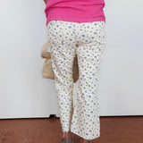 Person wearing a pink top and white floral pants on a plain background