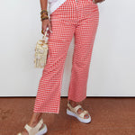Person wearing red and white checkered pants with a white top and beige sandals on a brown floor.