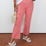 Person wearing red and white checkered pants with a white top and beige sandals on a brown floor.