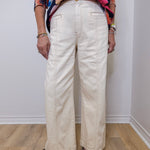 Person wearing a colorful floral top and white pants against a plain background