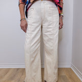 Person wearing a colorful floral top and white pants against a plain background