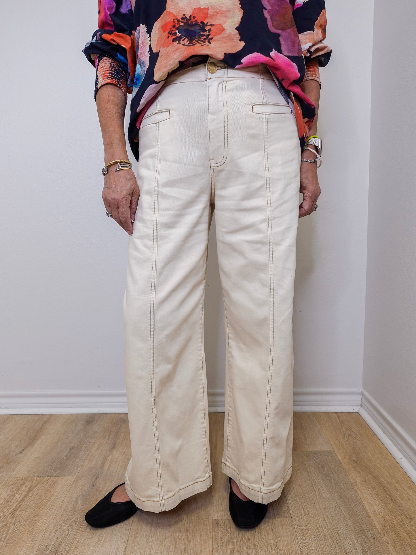 Person wearing a colorful floral top and white pants against a plain background