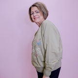 Woman wearing a green sweatshirt with floral embroidery against a pink wall.