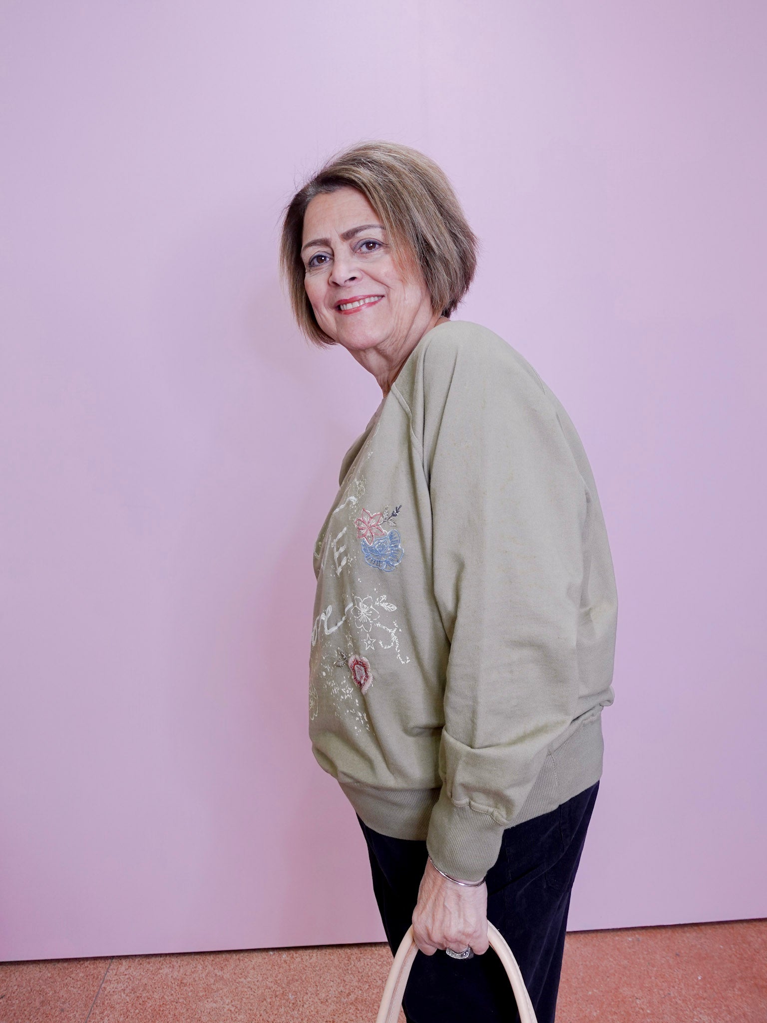 Woman wearing a green sweatshirt with floral embroidery against a pink wall.