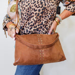 Person holding a brown leather handbag with decorative studs against a white background