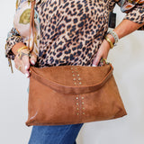 Person holding a brown leather handbag with decorative studs against a white background