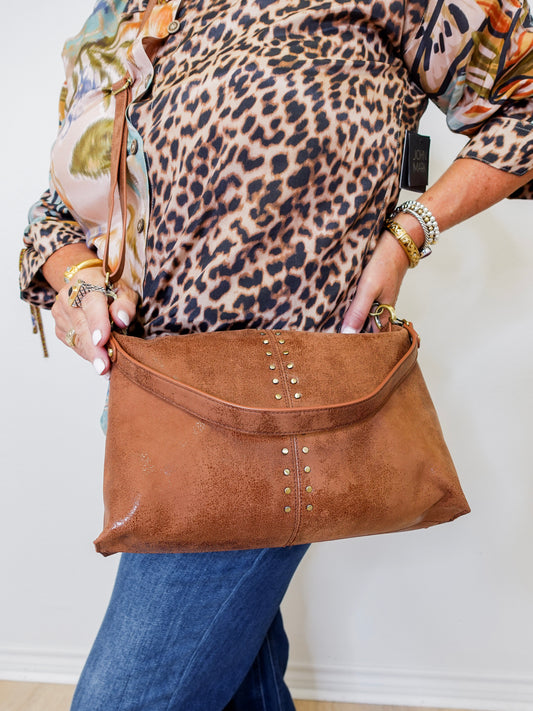 Person holding a brown leather handbag with decorative studs against a white background
