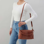 Person wearing a white long-sleeve top and blue jeans, holding a brown leather handbag against a gray background