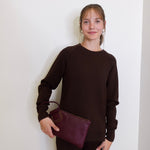 woman wearing the Maroon clutch bag with a ring handle on a light beige background