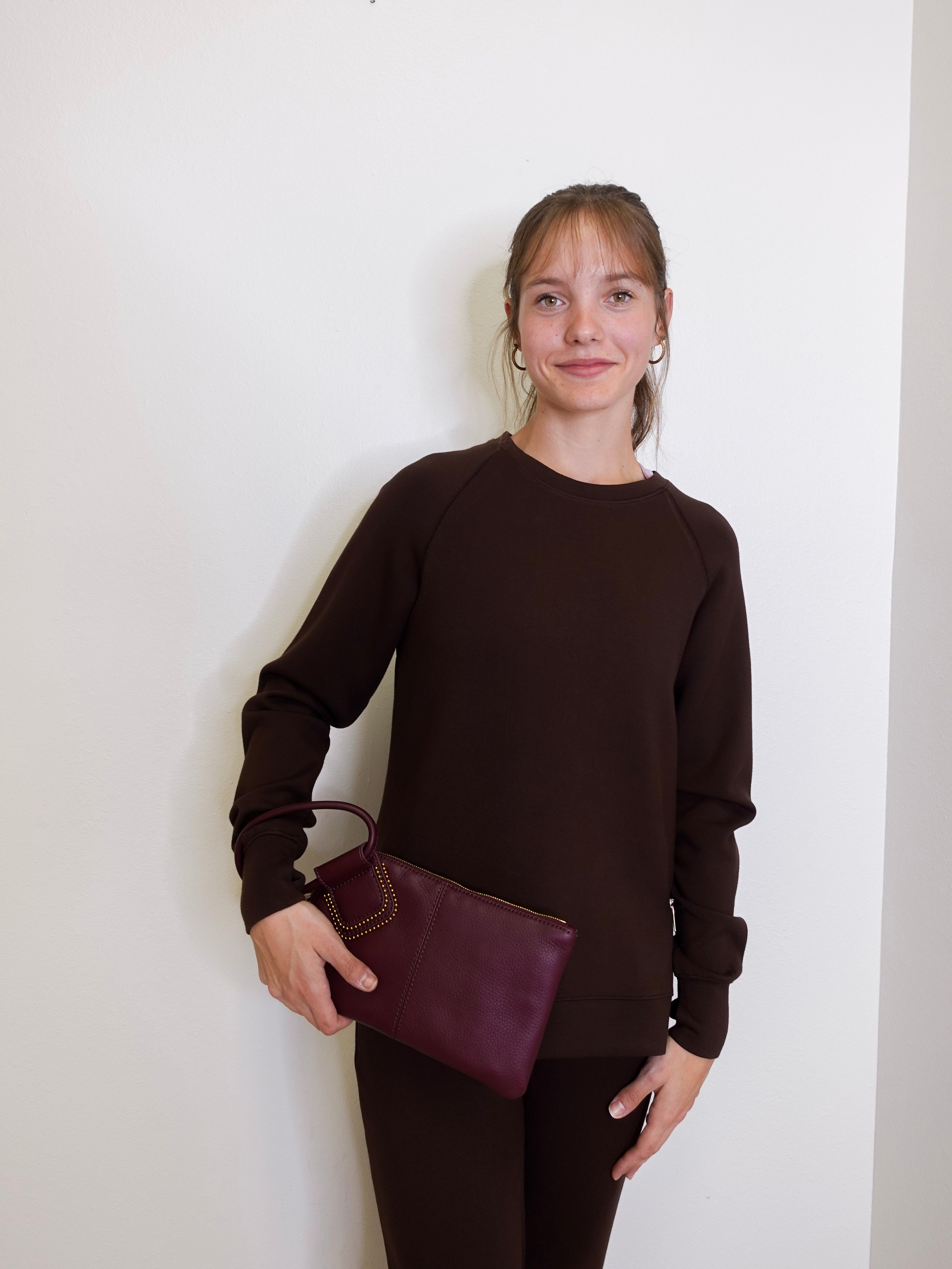 woman wearing the Maroon clutch bag with a ring handle on a light beige background
