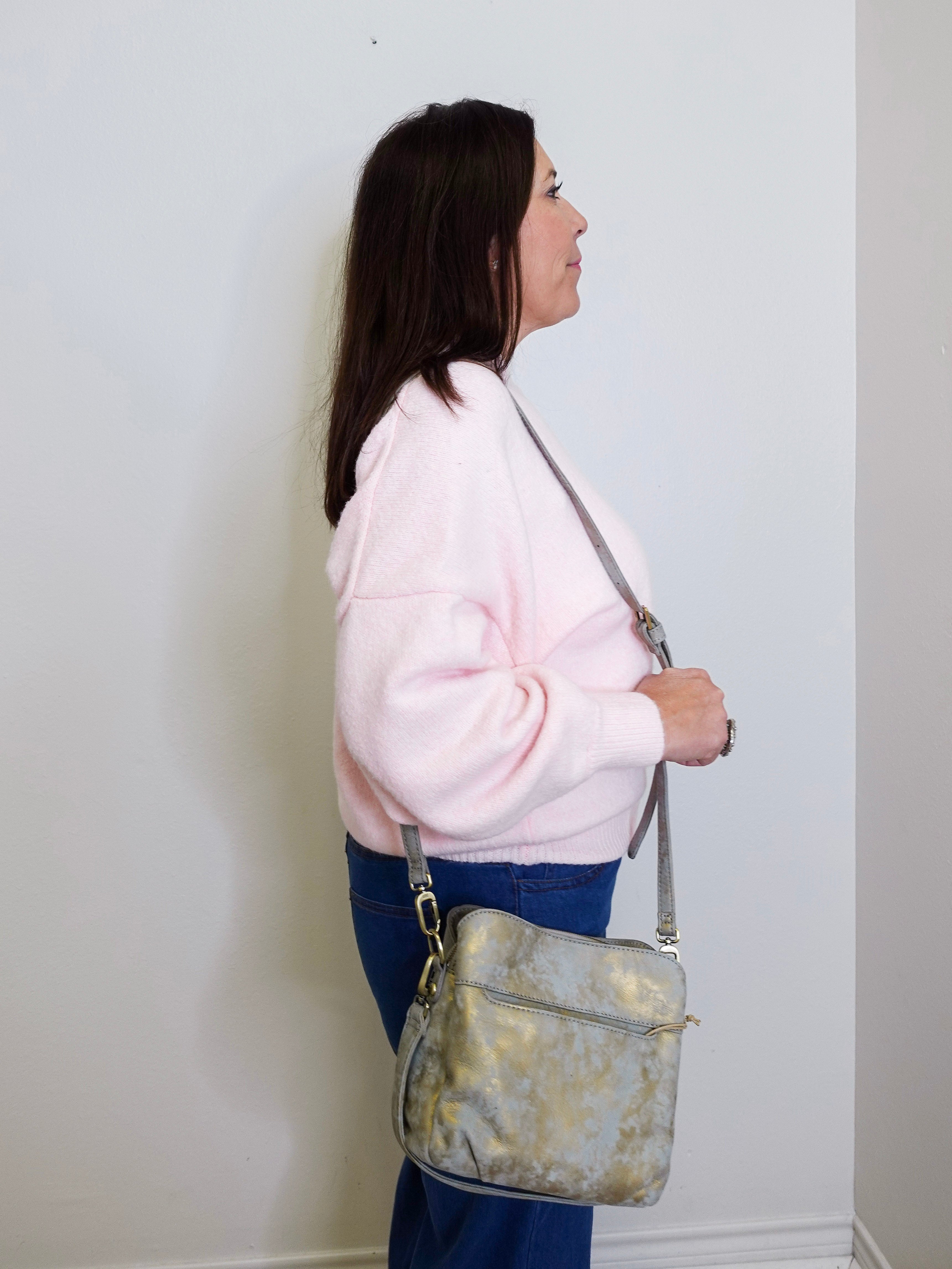 Woman holding a gray handbag against a white wall