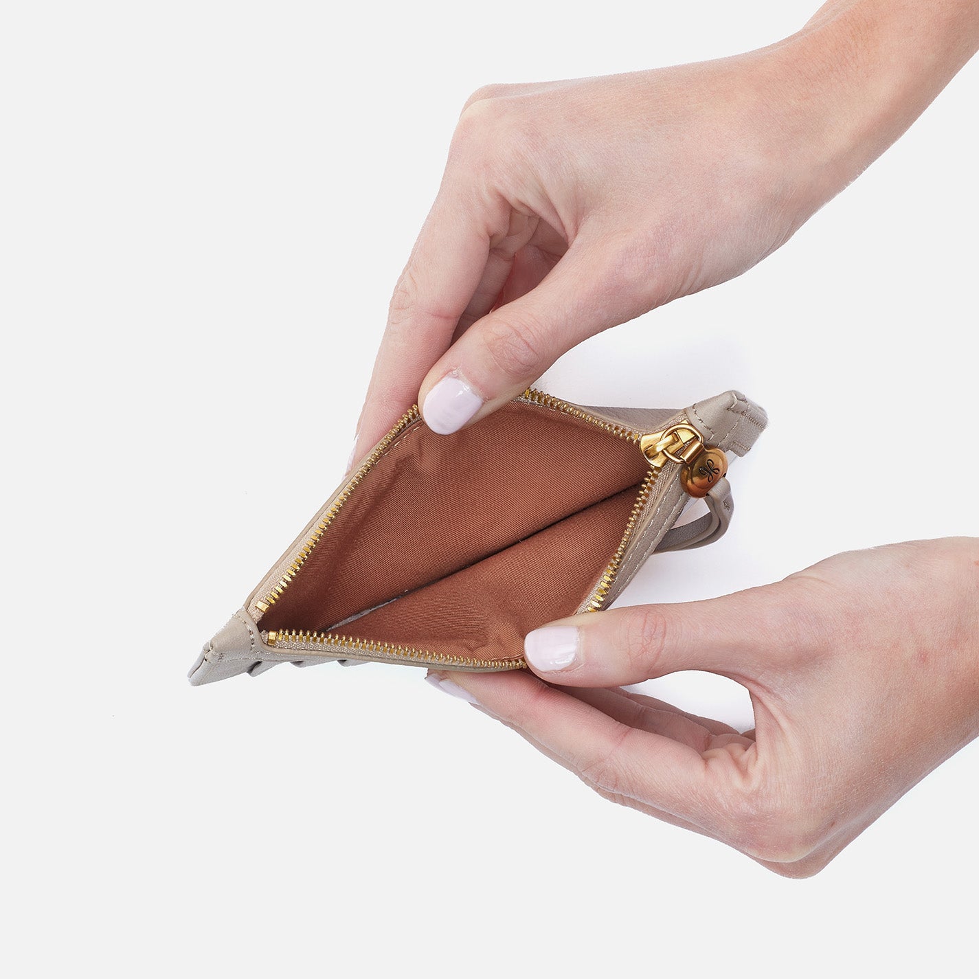 Hand holding an open beige wallet with a gold zipper on a white background