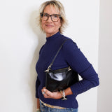 Woman wearing a blue sweater and glasses, holding a black handbag against a white background