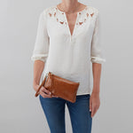 Person wearing a white blouse with bird patterns and blue jeans, holding a brown clutch against a gray background